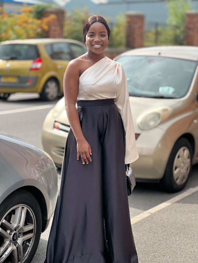 Woman in elegant one-shoulder satin dress, black skirt and ivory top, smiling outdoors