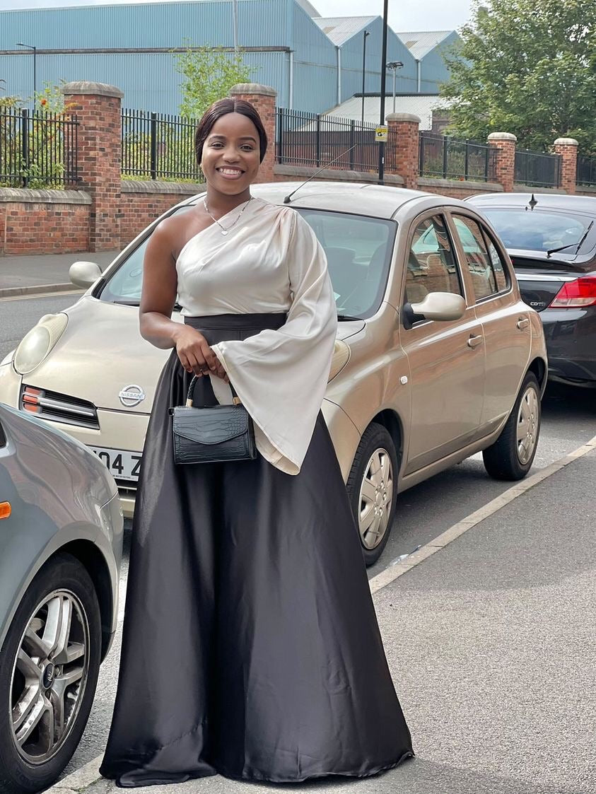 Woman in elegant one-shoulder satin dress with black skirt, standing on street.